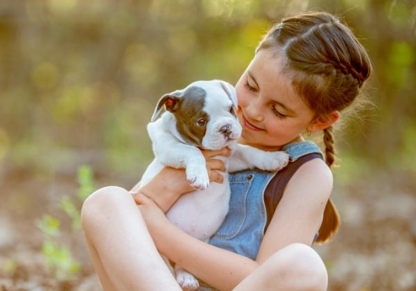 A young child wearing denim overalls gently holds a black and white puppy