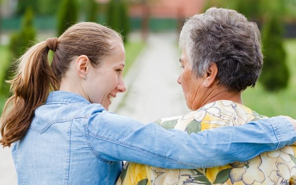 A younger person with an arm around an older person's shoulders